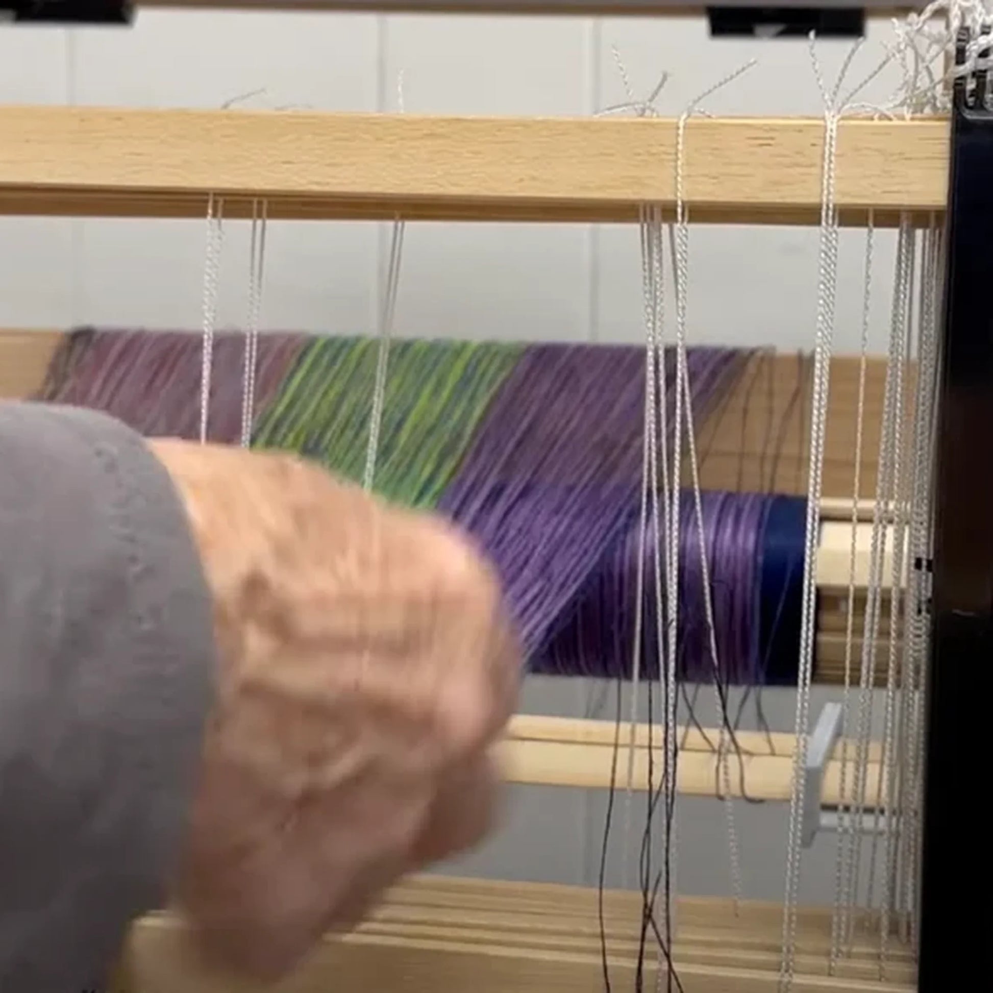 LoftyFiber Helping Hands am Louet Jane Tischwebstuhl – Hand führt lila-grünes Webgarn durch die Kettfäden beim Einfädeln