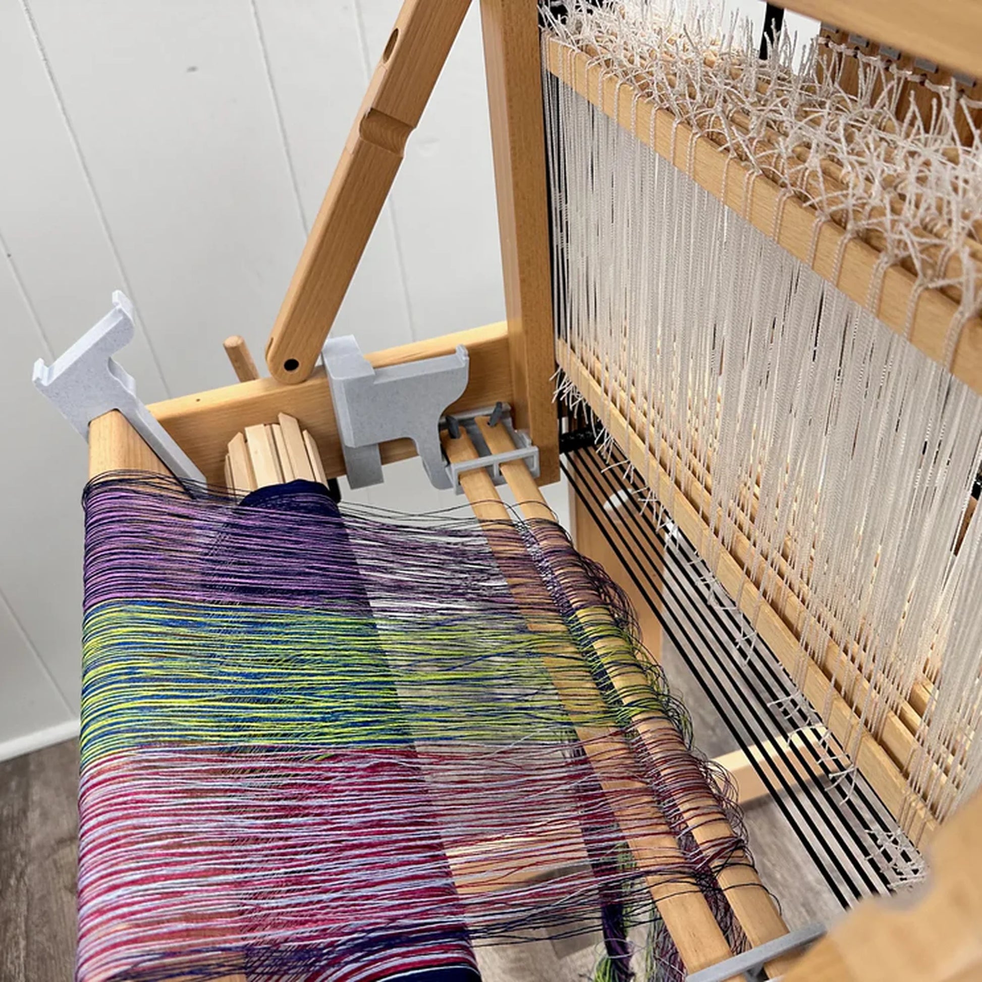 LoftyFiber Helping Hands am Louet Jane Tischwebstuhl – Draufsicht auf bunten Kettbaum mit lila-grünem Webgarn und montierten Helping Hands Halterungen